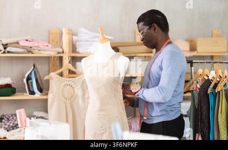 Male tailor sews new dress on a mannequin in sewing studio Stock Photo