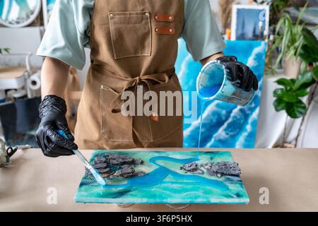 Woman creative artist working on handmade liquid art painting in home workshop at worktable. Stock Photo