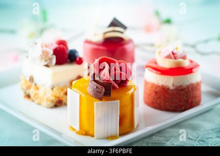 Various mini cakes on a white plate. Sweets decorated with fresh berries and flowers for holiday. Stock Photo