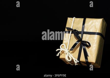 A present for a man, wrapped in brown paper and tied with 2 bows, one of black ribbon and the other of thick cotton cord, against a black background. Stock Photo