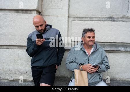 Two men waiting outdoors using smartphones Stock Photo