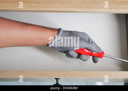 Person using screwdriver in kitchen cabinet Stock Photo