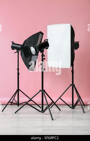 Professional studio lighting equipment with a softbox and strobe light on tripods against a pink background, the setup is positioned against a vibrant Stock Photo