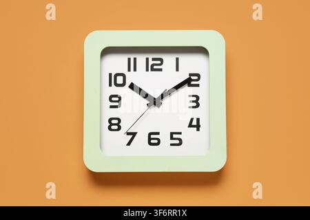 Square light green wall clock with black numbers and hands on an orange background, time management concept, the analog clock face shows the current t Stock Photo