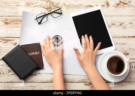 Person planning a global trip with a map, compass, passport, tablet, and coffee on a rustic wooden table Stock Photo