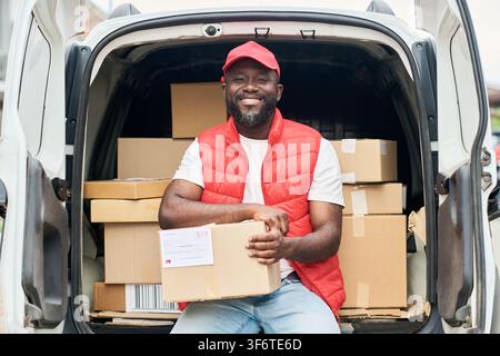 Portrait of Smiling Black Man Delivering Packages with Cargo Van Stock Photo