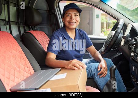 Portrait of Hispanic Female Courier Sitting in Delivery Van with Package Stock Photo