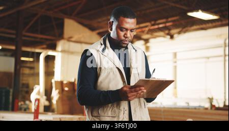 Carpenter, checklist or black man with clipboard in warehouse for wood production or inventory. Male person, carpentry or writing stock for lumber Stock Photo