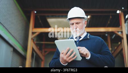 Civil engineer, online and man with tablet on construction site, scroll or renovation project on web. Confident, architect and mature person with Stock Photo
