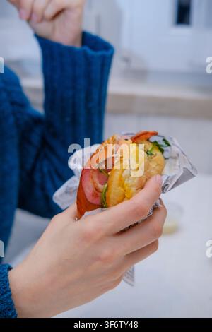 Woman holding a fast food breakfast sandwich wrapped in paper Stock Photo