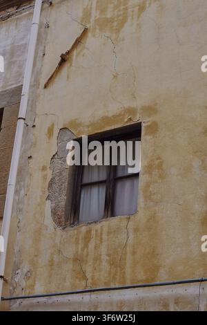 Weathered plaster façade with an old window and exposed stone surround on a historic building in Florence, Tuscany, Italy. Stock Photo