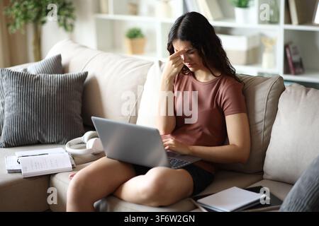 Teenage student suffering headache studying online sitting on a couch at home Stock Photo