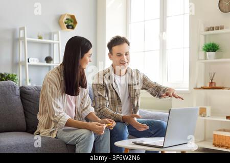 Couple sitting on sofa at home looking at laptop discussing ideas about interior design. Stock Photo