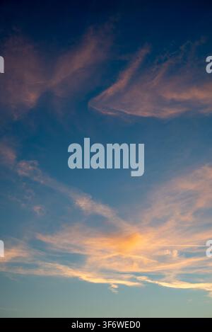 Vivid sky at sunrise or sunset, featuring thin, elongated clouds that create movement and texture against the cooler tones of the upper sky transition Stock Photo