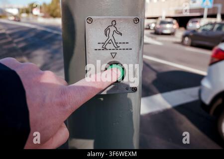 Hand pressing green button on a pedestrian crossing signal for urban road safety Stock Photo