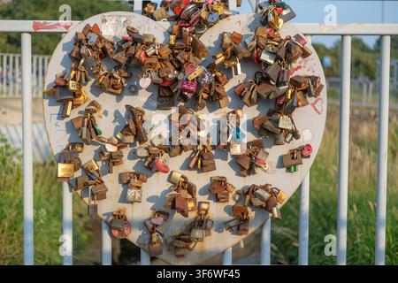 Hundreds of rusty metal padlocks are attached to a large white heart structure on a railing. Stock Photo