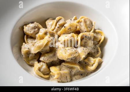 Italian stuffed pasta with creamy truffle sauce and black pepper, served in a white ceramic bowl. Traditional gourmet dish from central Italy. Stock Photo