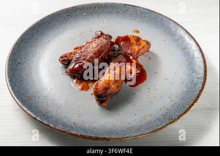 BBQ chicken wings glazed with rich barbecue sauce, roasted until crispy and caramelized, served as a savory appetizer on a blue ceramic plate Stock Photo