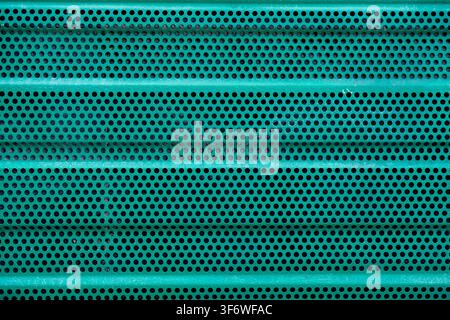 A green painted metal sheet is perforated with small circular holes. Stock Photo