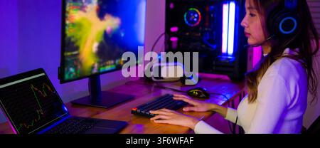 Asian professional gamer playing online video game on desktop computer PC screen display have colorful neon LED lights, young woman in gaming headphon Stock Photo