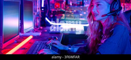 Woman hacker sitting in front of a computer typing on keyboard hacking servers in neon light, Female hacker breaks into data center, Gamer woman strea Stock Photo