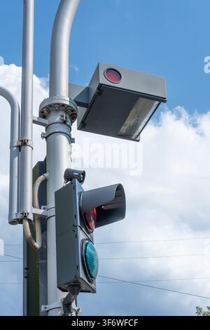 A traffic light and surveillance camera sensors are mounted on a metal pole against a blue sky. Stock Photo