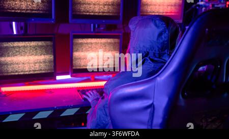 Back view of female hacker breaks into data center, Blockchain cyber attack, Woman hacker wear hood sit front computer typing on keyboard hacking serv Stock Photo
