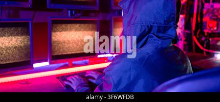 Woman hacker wear hood sit front computer typing on keyboard hacking servers in neon light, Gamer woman streaming game online dark room, Female hacker Stock Photo