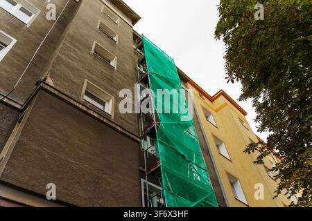 Building facade undergoing renovation with green protective safety netting. Construction scaffolding for maintenance or exterior repair project Stock Photo