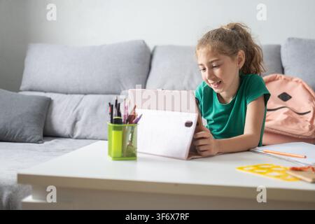 Happy elementary school girl smiling while using a digital tablet at home. Stock Photo