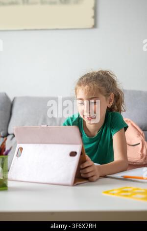 Happy elementary school girl smiling while using a digital tablet at home. Stock Photo