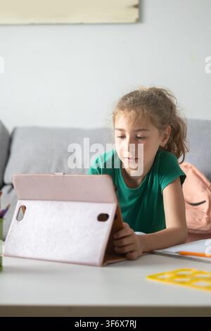 Focused school-age girl using a digital tablet while studying at home. Stock Photo