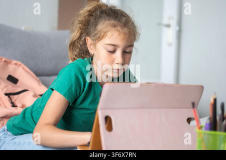 Focused school-age girl using a digital tablet while studying at home. Stock Photo
