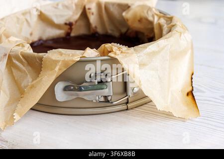 Freshly baked brownie in parchment lined springform pan with clasp on a white wooden table. Selective focus Stock Photo