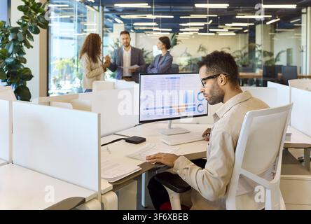 Young analyst working with financial spreadsheet at desktop in collaborative office Stock Photo