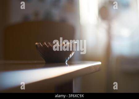 A close-up shot of a small glass bowl filled with delicious crunchy peanuts placed on a smooth wooden table inside a cozy room with soft natural light Stock Photo