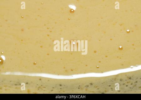 Macro close-up shot showcasing the fine texture of whipped beaten egg yolk with tiny air bubbles trapped inside the rich yellow liquid during baking p Stock Photo