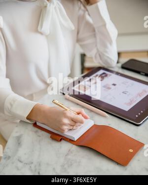 Woman Writing Notes on Notepad Beside Digital Tablet Stock Photo
