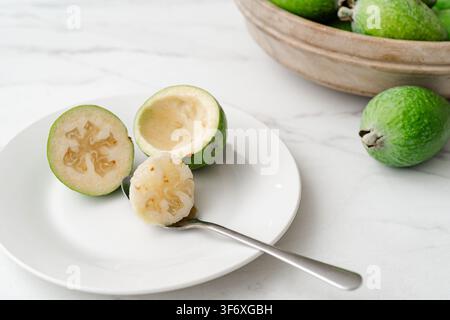 Eating feijoa fruit with a spoon on a white plate Stock Photo