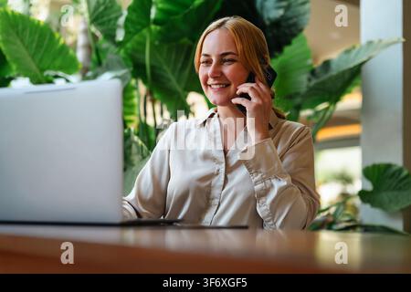Smiling woman talking on her phone using laptop Stock Photo