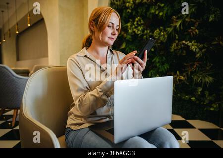 Woman using smartphone while working in modern lobby Stock Photo