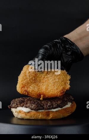 Chef putting deep fried cheese patty onto a grilled beef burger Stock Photo