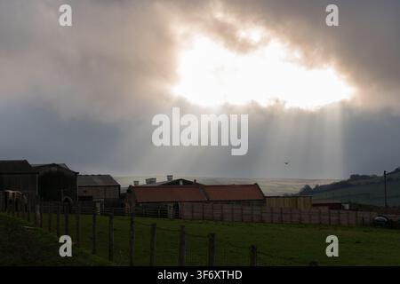 Crepuscular rays illuminate a farm near Staithes, North Yorkshire, as sunlight breaks through dramatic clouds over the English coast. Stock Photo