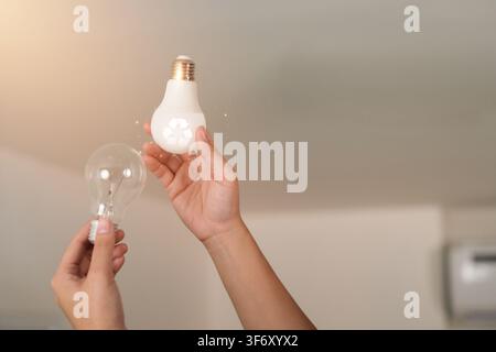Hands changing incandescent bulb to energy efficient LED light bulb for power saving concept Stock Photo