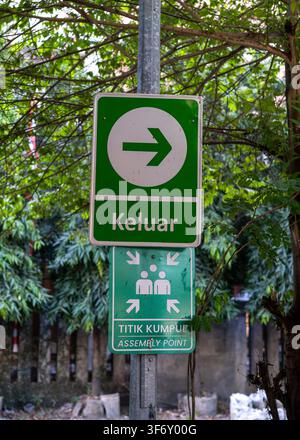 A green bilingual safety sign showing Exit Keluar and Assembly Point Titik Kumpul at the back exit of Hokky Merr in Surabaya, Indonesia. Stock Photo