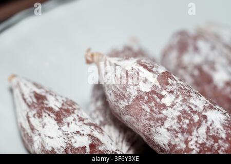Macro view of gourmet dry cured sausages with natural white mold coating arranged together on a light ceramic plate, highlighting traditional meat pre Stock Photo