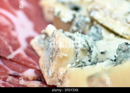 Close-up view of creamy blue cheese slices with blue mold alongside thinly sliced cured meat arranged on a platter for a gourmet appetizer snack. Stock Photo