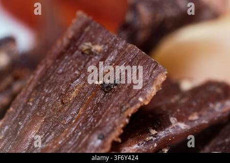 Macro close-up shot of savory beef jerky strips showing fibrous meat texture and black pepper seasoning. Delicious dried meat snack ready to eat. Stock Photo