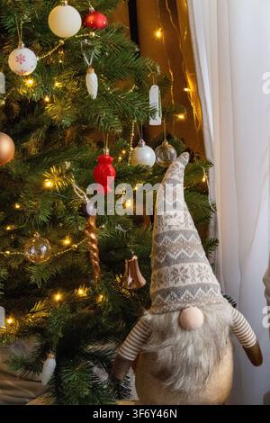 Christmas tree decorated with ornaments baubles and warm string lights glows in festive home setting. Concept of traditional holiday decoration and wa Stock Photo