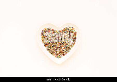 Colorful sugar confectionery stars arranged in a heart shaped plate on a white background with copy space. Top view Stock Photo